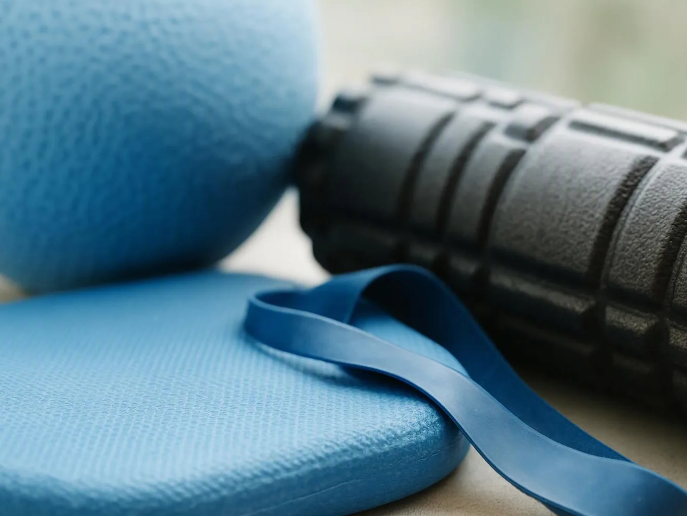 A blue exercise mat and resistance band lie beside a black foam roller on a floor