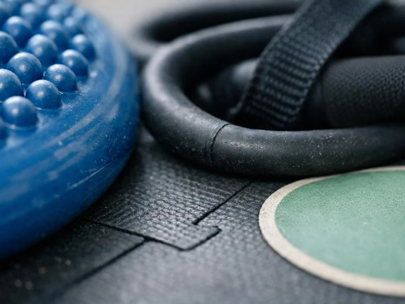 Close-up of blue massage balls, black straps, and a green mat on a textured workout surface